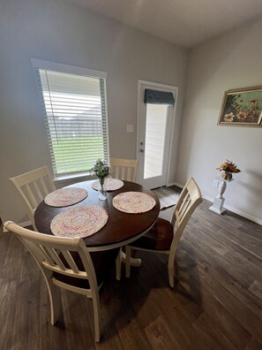 Enjoy meals in this cozy dining area with a round table and six chairs, surrounded by a beautiful floral painting and a lush green plant.