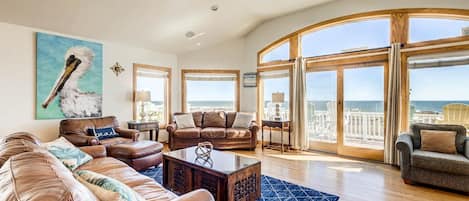 A spacious living room with leather sofas, a coffee table, and large windows offering a view of the ocean.