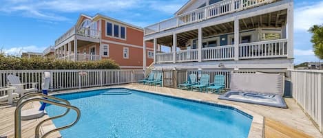 A pool area with a wooden deck, lounge chairs, and a two-story building with balconies.