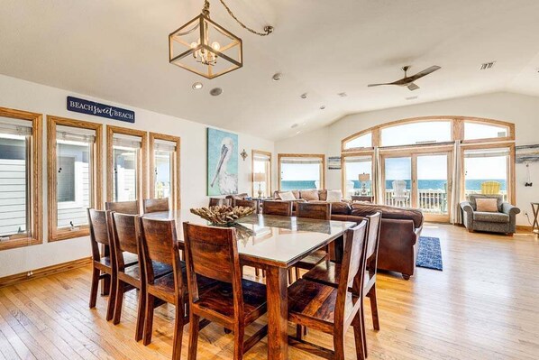 A spacious living area with a dining table, chairs, a sofa, and a view of the ocean. - Wink Beach | Oceanfront | Private Pool, Hot Tub, and Dog Friendly (Nags Head)