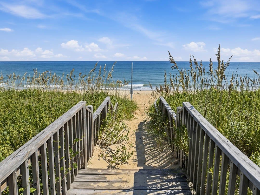 Une promenade en bois qui mène à une plage d’où l’on a une vue dégagée sur l’océan.