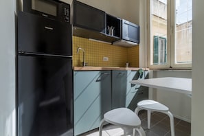 Una cocina compacta con un refrigerador negro, un microondas y un lavamanos. Hay dos taburetes blancos y una mesa pequeña.