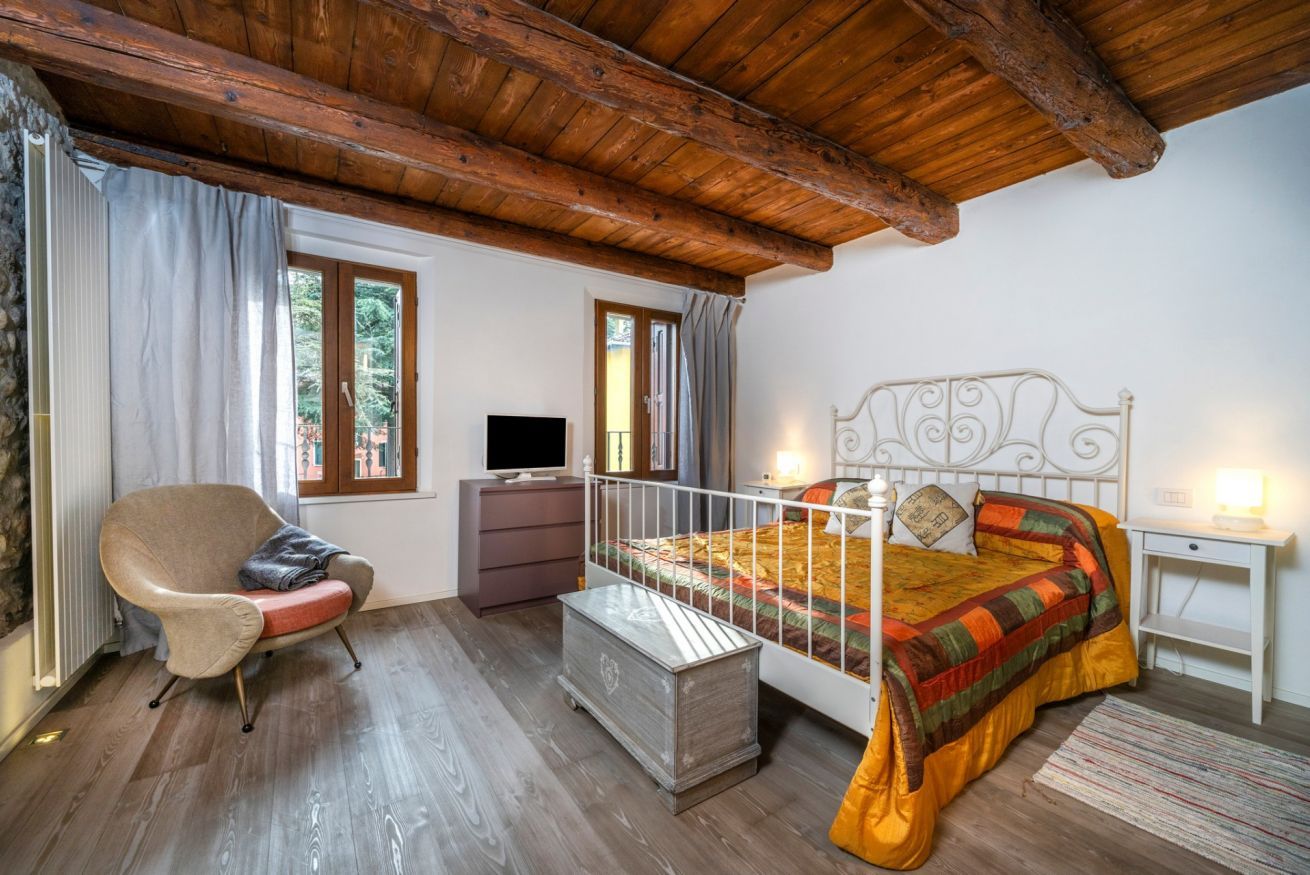 A bedroom with a bed, a chair, a dresser, a television, and a window.