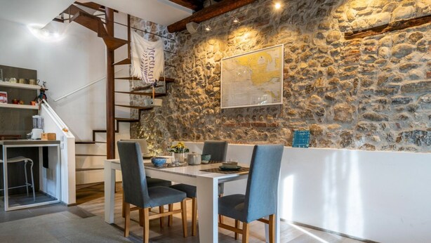 A dining area with a stone wall, wooden beams, and a white table. - GuestHost - Jacaranda Comfy House (Udine)