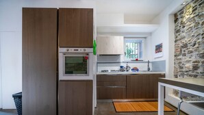 A modern kitchen with a built-in oven, wooden cabinets, a stone wall, and a window. - GuestHost - Jacaranda Comfy House (Udine)