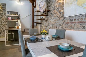 A dining area with a stone wall, a map, a staircase, and a table set with bowls and a pitcher. - GuestHost - Comfortable Jacaranda House (Udine)