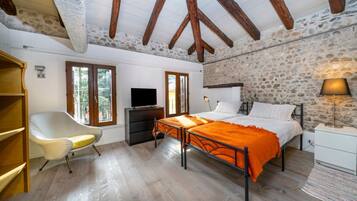 Ein Schlafzimmer mit Steinwand, Holzbalken, einem Bett, einem Sessel, einem Fernseher und einer Lampe.