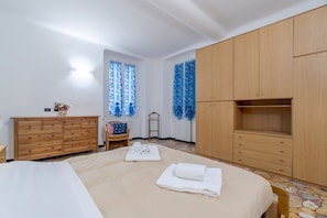 Une chambre à coucher avec un lit, une armoire en bois et une petite table sur laquelle est posé un vase.