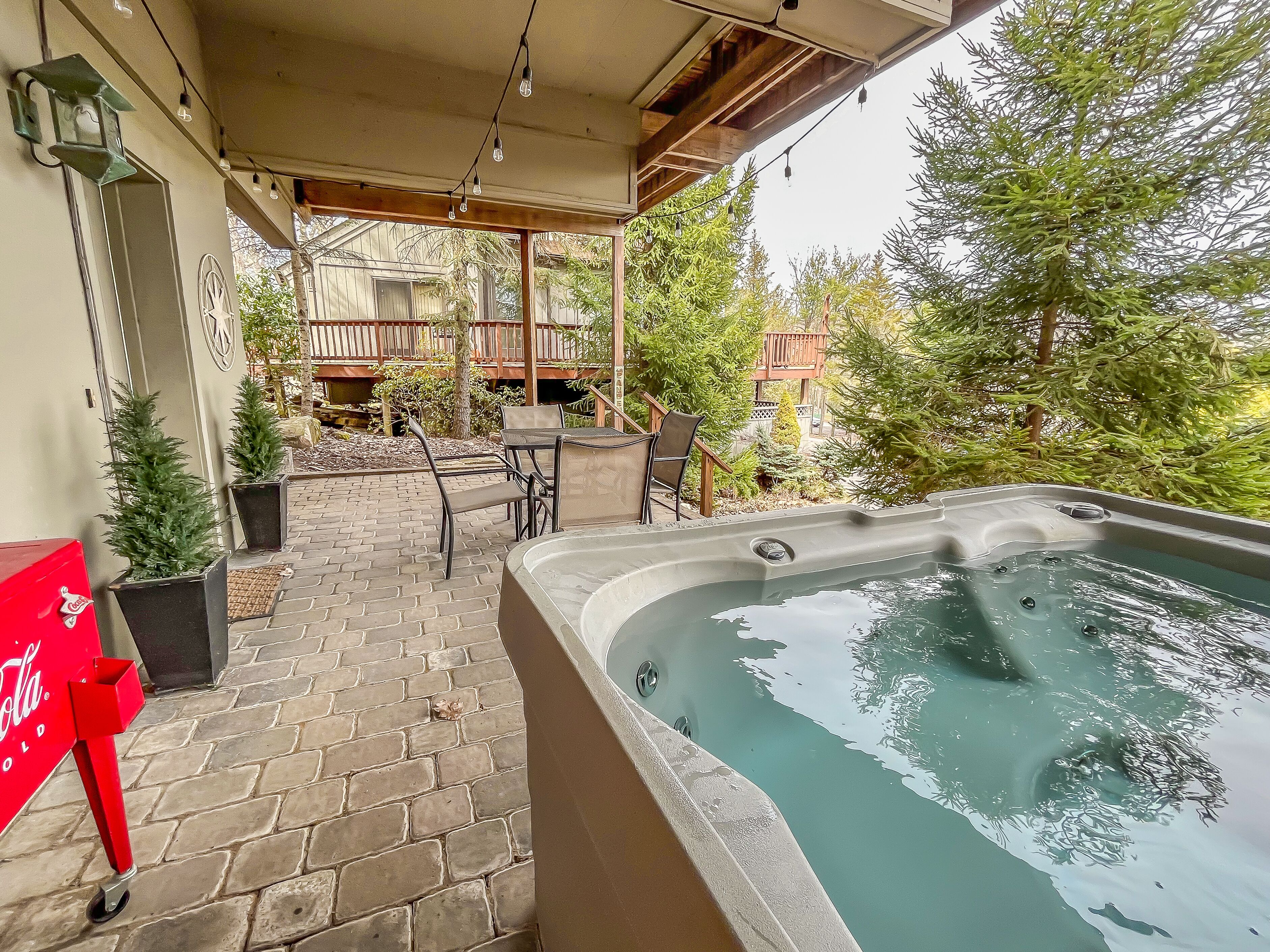 A hot tub area with a brick patio, outdoor furniture, and a Coca-Cola cooler.