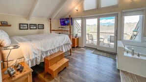 Een slaapkamer met een groot bed, een houten bankje en een televisie aan de muur.