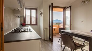 Una cocina con estufa a gas, una olla roja y un ventanal. Hay una zona de comedor con mesa y sillas.