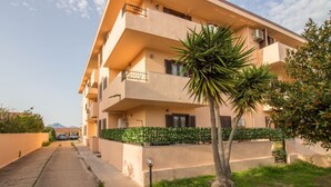 Un edificio residencial de varios pisos con balcones, un camino pavimentado y un jardín bien cuidado con una palmera.