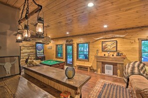 A wooden interior with a pool table, dartboard, and a fireplace.