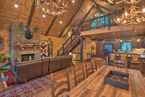 A rustic interior with a stone fireplace, wooden ceiling, and a staircase.
