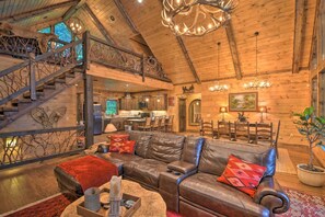 A spacious living area with a leather sofa, wooden staircase, and a chandelier.