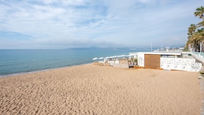 A beach with a white building, palm trees, and a clear sky. - Appartement Dollia - Welkeys (Cannes)