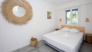 A bedroom with a bed, a round mirror, a picture on the wall, and a window with a view of trees. - Appartement Dollia - Welkeys (Cannes)