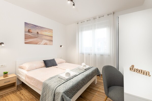 Une chambre bien rangée, avec un lit, une table de chevet, une chaise et un tableau accroché au mur.