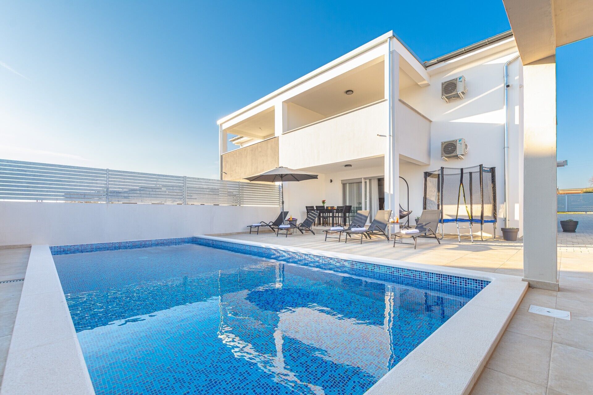 A rooftop pool area with a clear blue pool, lounge chairs, and a covered seating area.