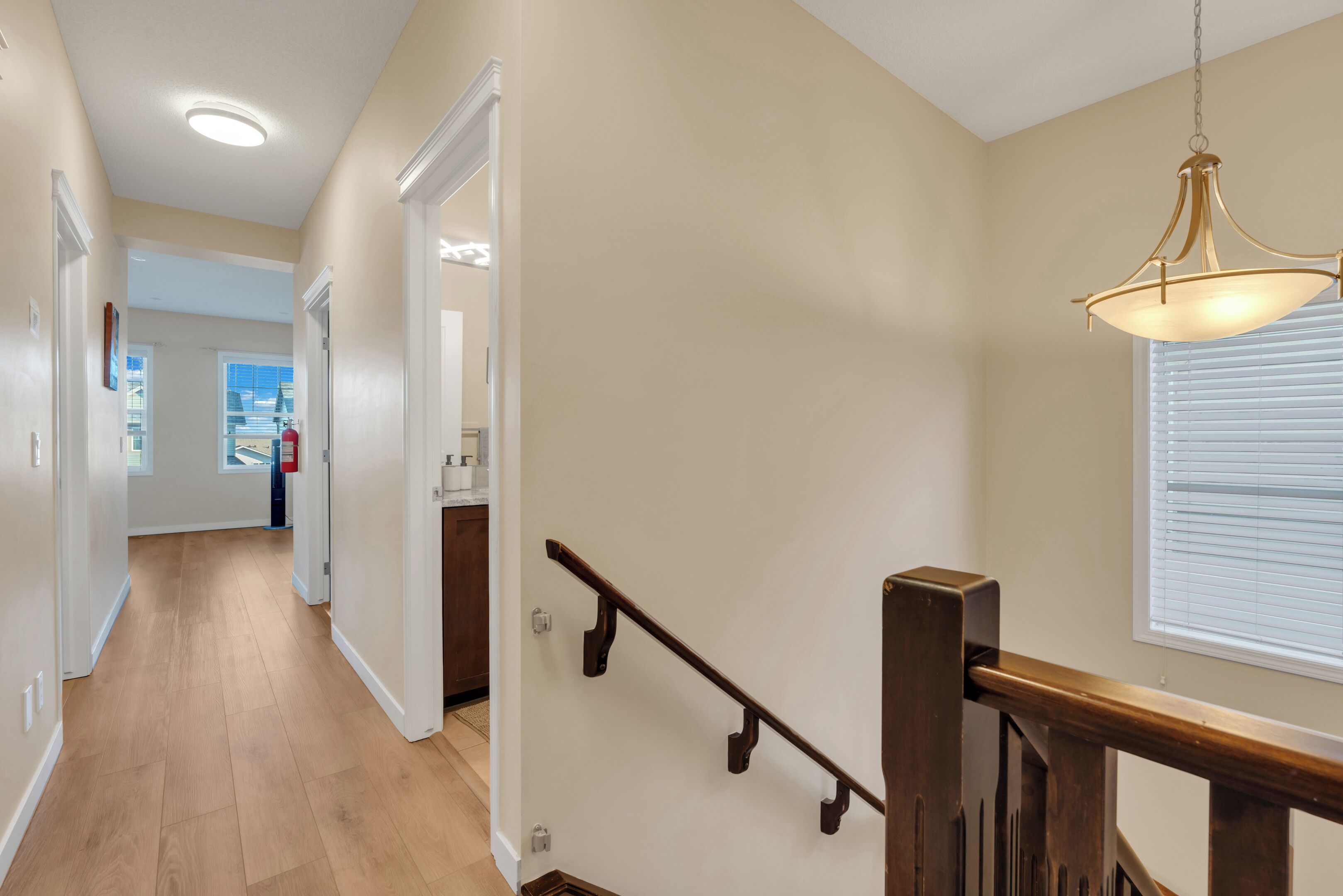 A hallway with wooden flooring, a wooden staircase with a handrail, and a ceiling light fixture.