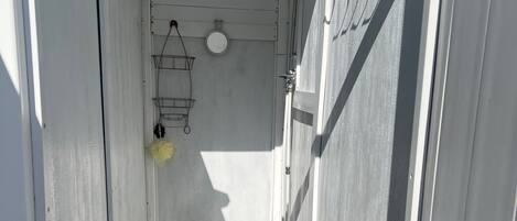 A narrow corridor with a white door at the end, a small window, and a metal rack with a yellow item hanging from it.