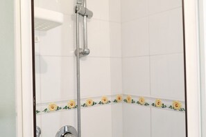Eine Dusche mit Handbrause, weißen Fliesen und einem Blumenmuster an der Wand.