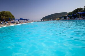 Ein Schwimmbecken mit klarem, blauem Wasser, umgeben von Liegestühlen und Sonnenschirmen.