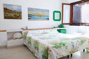 Ein Schlafzimmer mit einem Bett, einem Nachttisch, einer Kommode, einem Fenster und zwei Bildern an der Wand.