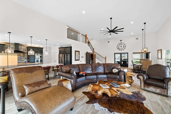 A spacious living area with a leather sofa, a wooden coffee table, and a large clock on the wall. - Perfect Couple’s Getaway in Luckenbach Tx Hot tub Pool (Fredericksburg)