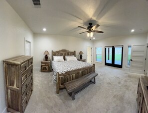 A bedroom with a wooden bed, bedside tables, a bench, a ceiling fan, and a view of the outside. - Perfect Couple’s Getaway in Luckenbach Tx Hot tub Pool (Fredericksburg)