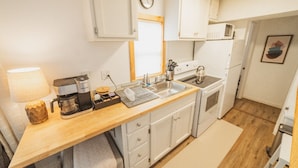 A compact kitchen with white cabinets, a wooden countertop, a coffee maker, a sink, and a microwave.