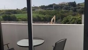 A balcony with a table and two chairs, overlooking a green landscape with buildings in the distance.