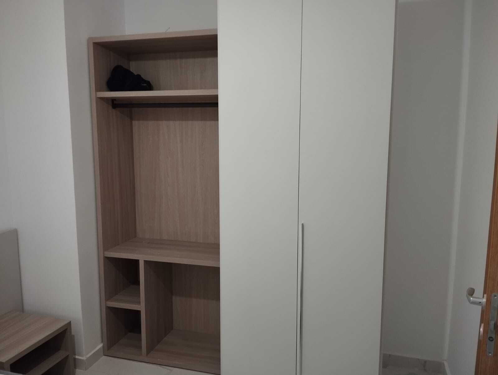 A room with a wooden wardrobe, a small table, and a door.