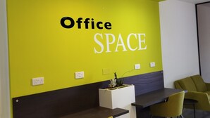 An office space with a bright green wall, a white reception desk, and two yellow chairs.