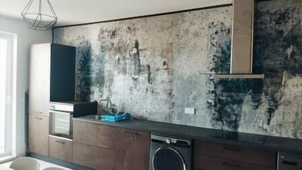 A modern kitchen with a distressed wall, built-in appliances, and a hanging light fixture.