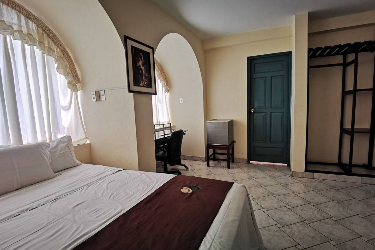 A hotel room with a bed, a desk, a chair, a wardrobe, and a door.