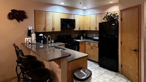 A modern kitchen with wooden cabinets, a granite countertop, a stainless steel trash can, and a built-in microwave. - Experience Comfort and Convenience at Kendall 337, 2-bedroom condo in the heart of Purgatory Village (Durango)
