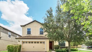 A two-story house with a garage, a well-maintained lawn, and a tree in front. - Splendor Retreat| 6BR Villa w/ Kid's Room & Pool (Davenport)