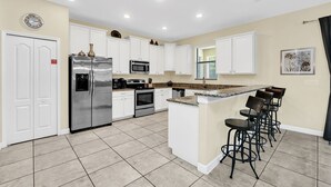 A modern kitchen with white cabinets, stainless steel appliances, and a central island with bar stools. - Splendor Retreat| 6BR Villa w/ Kid's Room & Pool (Davenport)