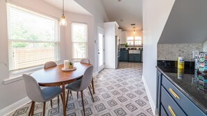 Un coin repas avec une table ronde et des chaises, une cuisine avec des meubles sombres et un plan de travail, et un revêtement de sol à motifs.