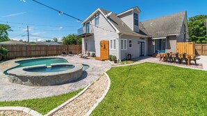 Une maison à deux étages avec un jardin comprenant une piscine, une terrasse en bois et un patio aménagé avec du mobilier d’extérieur.