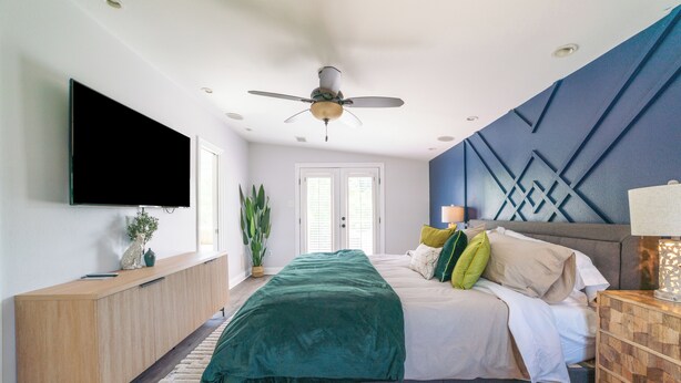 Une chambre moderne avec un lit, un ventilateur de plafond, une télévision et une console en bois.