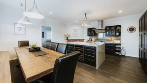 A modern kitchen with a wooden dining table, black leather chairs, pendant lights, and a built-in island with a sink.