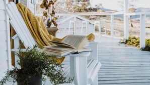 A white porch with a white chair and a book on it.