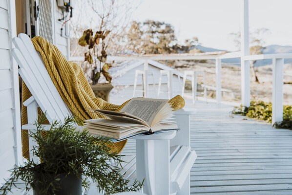 A white porch with a white chair and a book on it. - A perfect place to rest, relax and reconnect with friends or family. (Meroo)