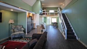 A spacious living area with a sofa, a patterned armchair, and a red rug. A staircase leads to an upper level.
