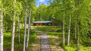 Une cabane en bois avec un toit vert, entourée de bouleaux, et un chemin de gravier menant à celle-ci.