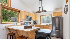 Une cuisine moderne avec des meubles en bois, un îlot central, un réfrigérateur en acier inoxydable et un four à micro-ondes.