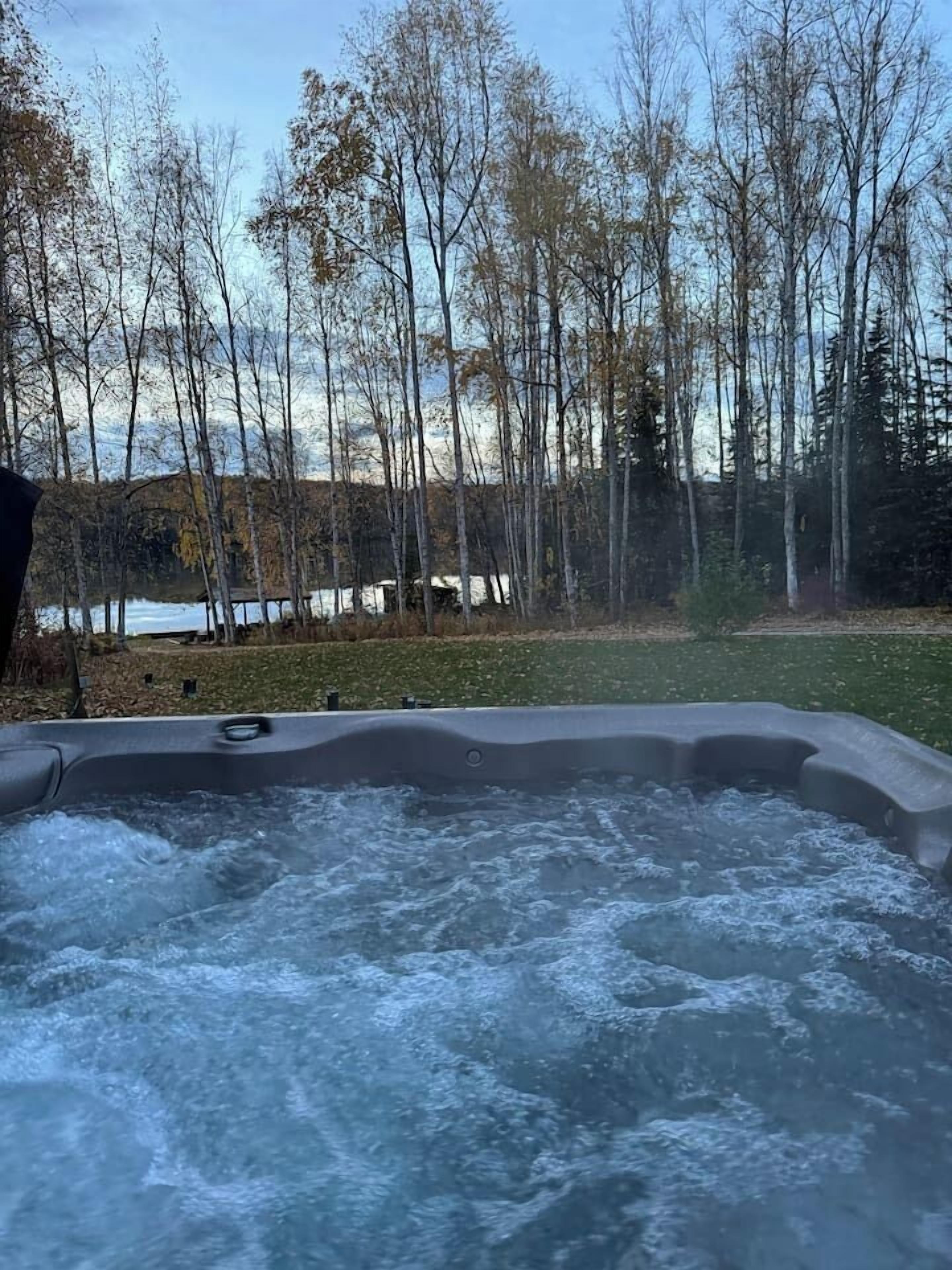 A hot tub with a view of a forest and a lake.