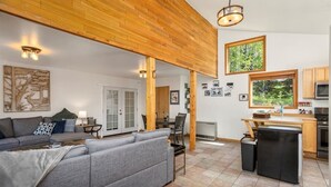Un salon moderne avec un canapé gris, un plafond en bois et un coin repas comprenant une petite cuisine.